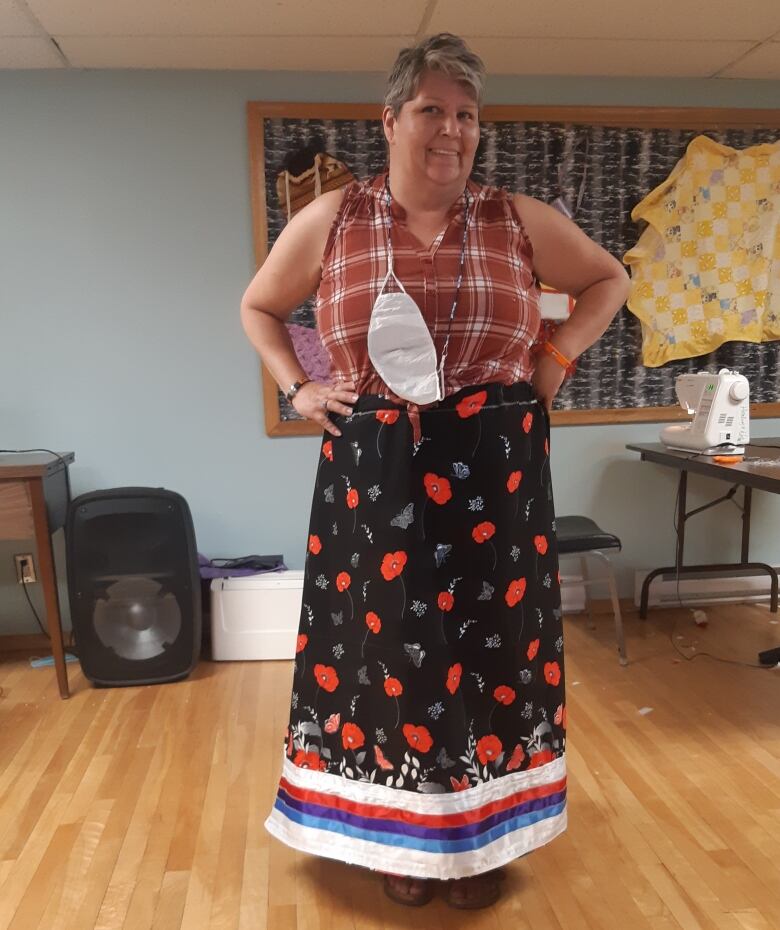 Woman wears homemade ribbon skirt with black and red poppy fabric, with a sewing machine in background.