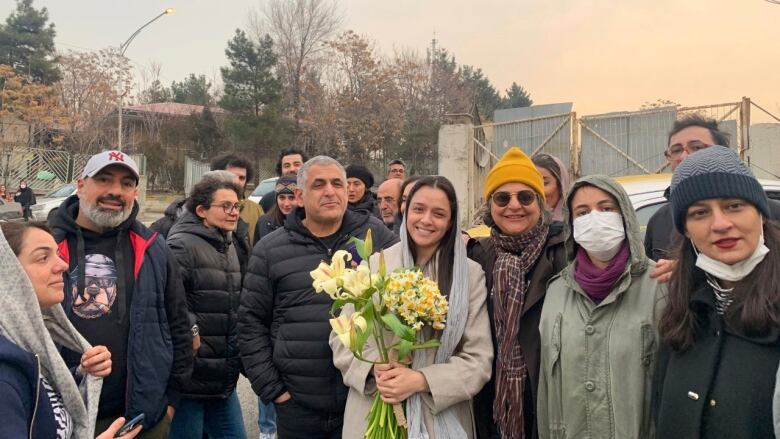 A woman holding yellow flowers poses among friends.