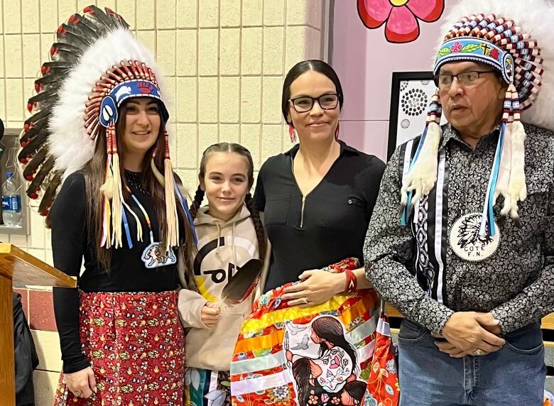 A young girl and a woman pose with another woman and a man, both of whom are wearing Indigenous headdresses.