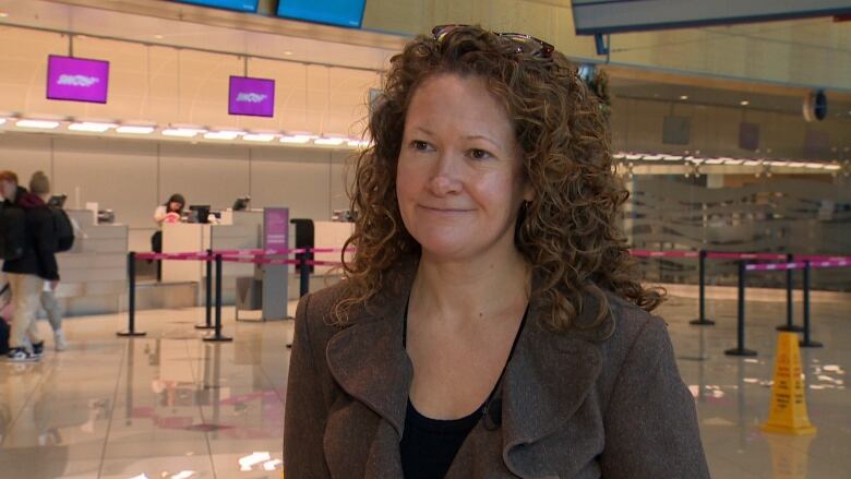 A woman wearing a grey coat standing in an airport terminal. 