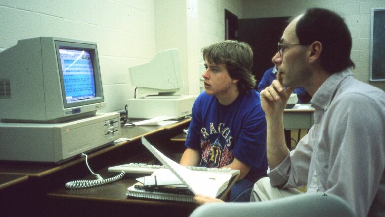 A student and teacher look at an old computer screen in 1993.