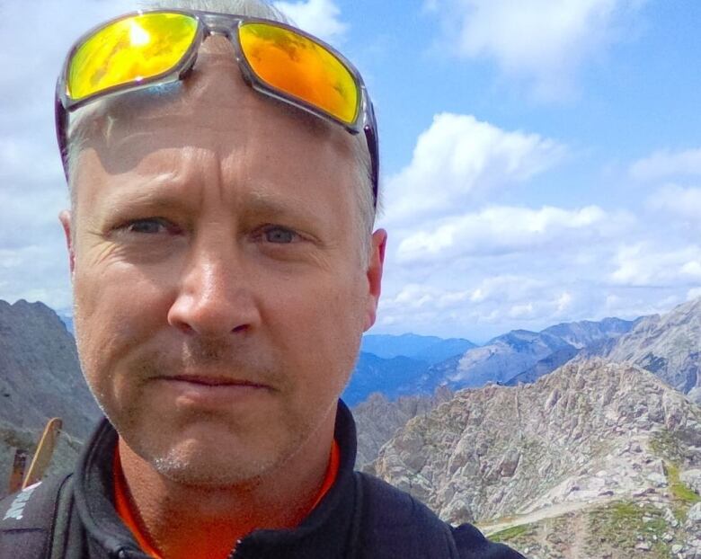 Portrait of man wearing ski goggles on his forehead and standing on top of a mountain.