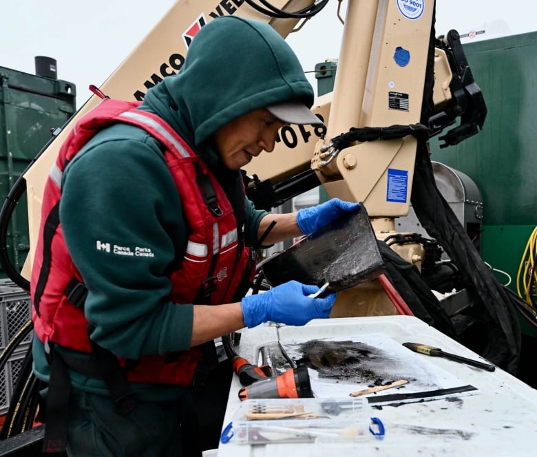 A man wearing warm clothes, a lifejacket and gloves handles an old looking artifact.