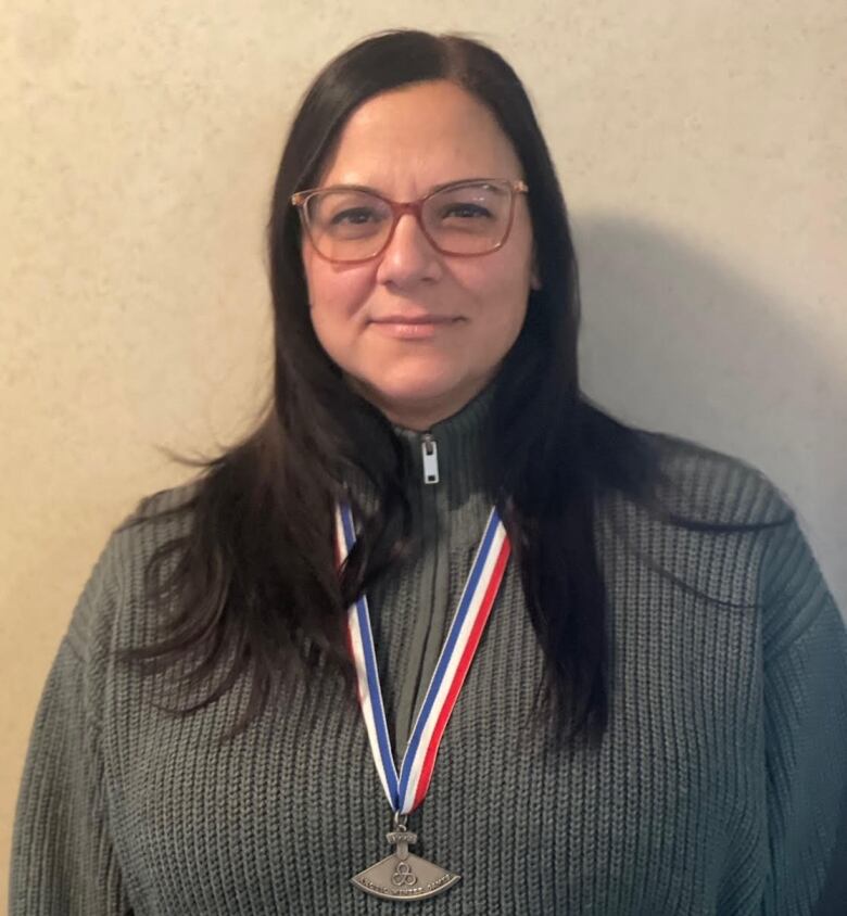 A woman with long, black hair stands for a portrait. She's wearing a silver medal. 