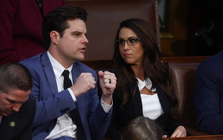 Woman with dark hair and glasses speaks to dark-haired man who is gesturing with clenched fists. 