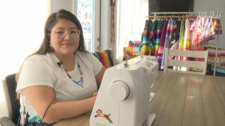 A woman in a white t shirt sits at a sewing machine. 