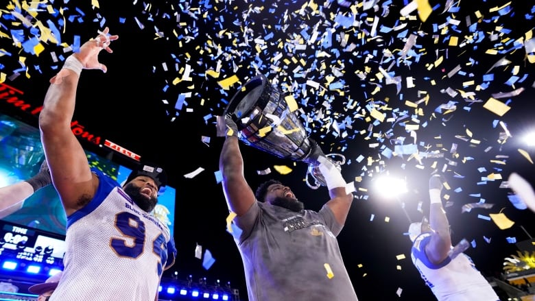 Three football players are surrounded by confetti and holding a trophy