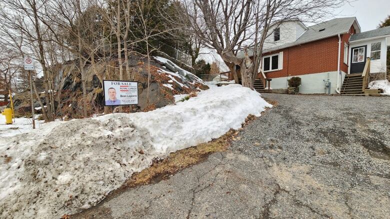 A for sale sign on a snowy lawn in front of a single family home.