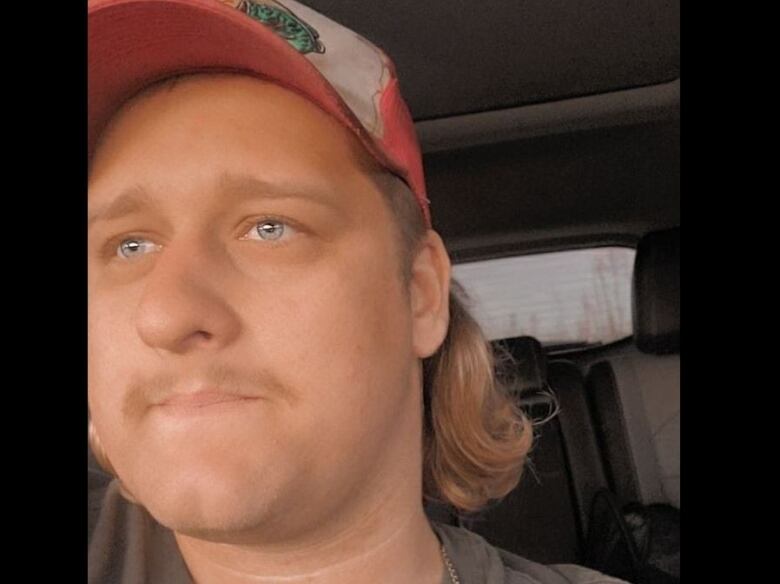 A man in a ballcap and mullet sits inside a vehicle. 