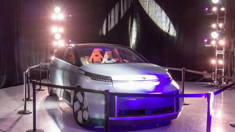 A futuristic-looking car surrounded by stanchions in a show room.