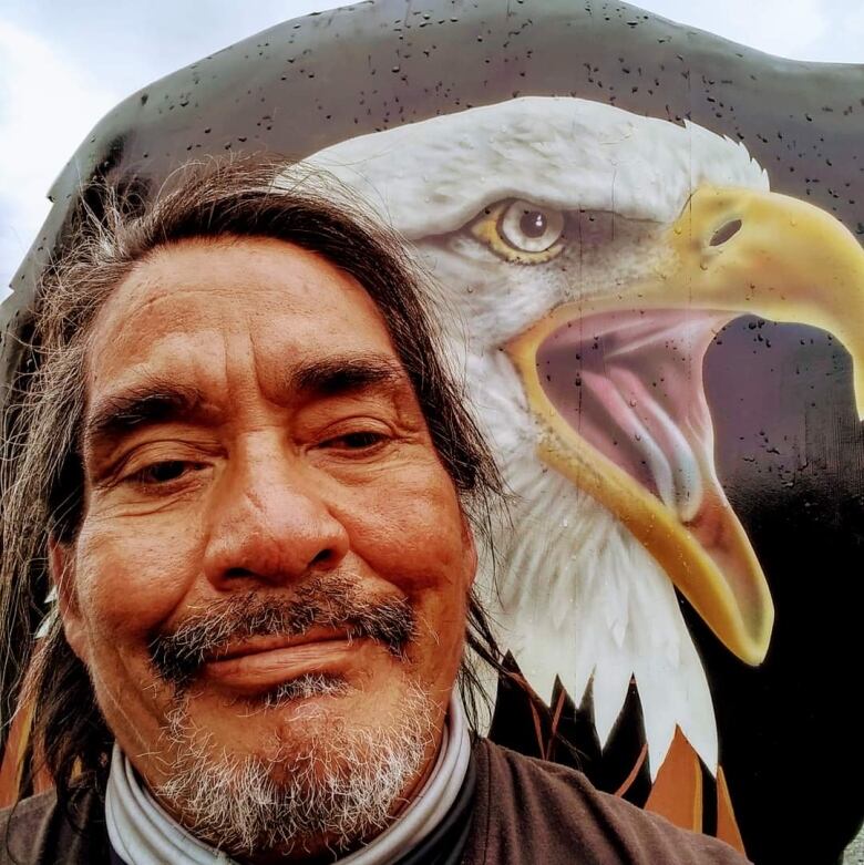 A man takes a selfie in front of an eagle mural.