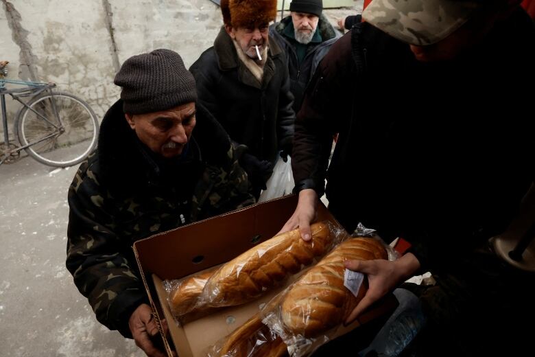 An individual is handed 2 loaves of bread at the front of a line of several men. 