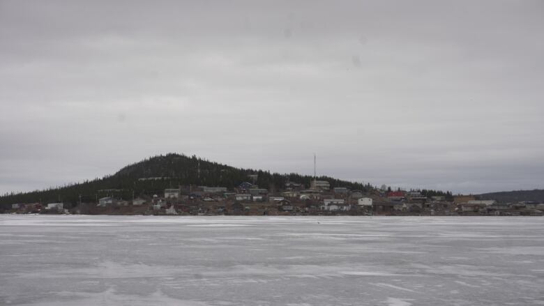 A frozen lake sits before a small community that has a hill in the background. 