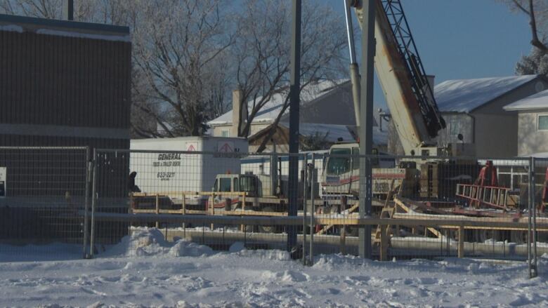 This picture shows a construction site with a crane and heavy machinery behind a metal fence.