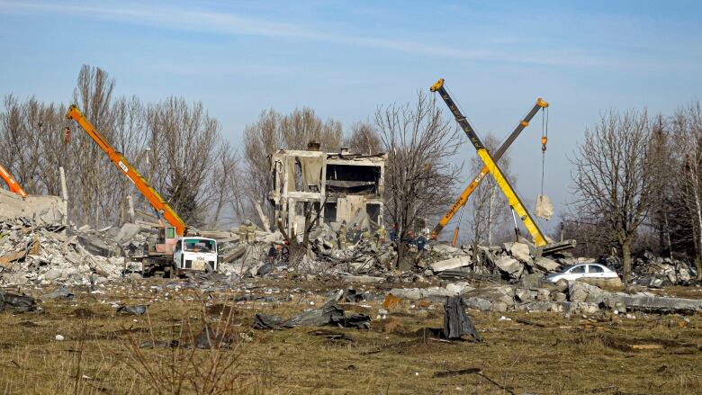 People and heavy machinery remove debris from a destroyed building.