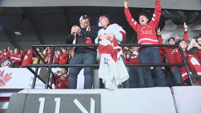 People wearing Team Canada memorbilia cheer and clap in an arena.  