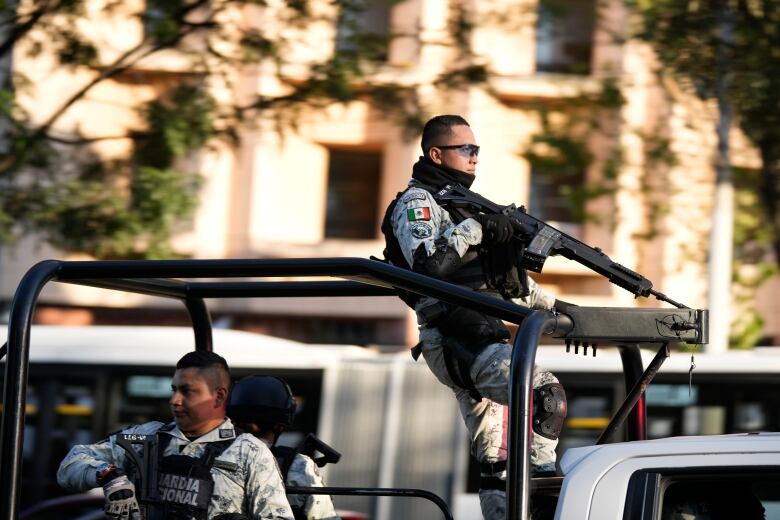 Men holding machine guns wait in a jeep outside a building