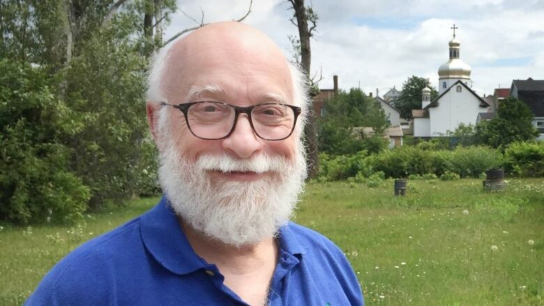 A man stands in a field next to a Ukrainian catholic church.