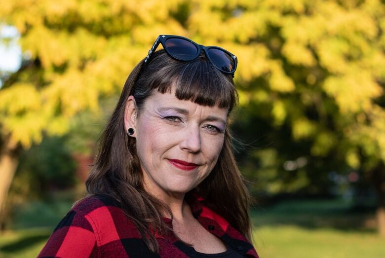 A woman in a plaid shirt stands outside by a tree 