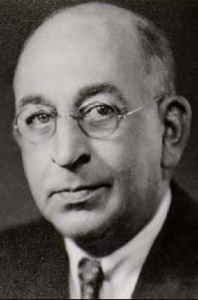 An old photograph of a middle-aged man, balding with circular wire-framed glasses.