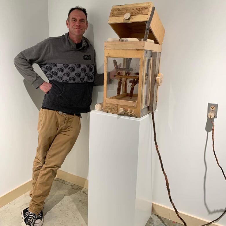 Yellowknife artist Mike Mitchell stands next to his wooden replica of a hot dog machine, one of the installations currently on display in the visitor centre gallery's show YellowknifeNOW! 