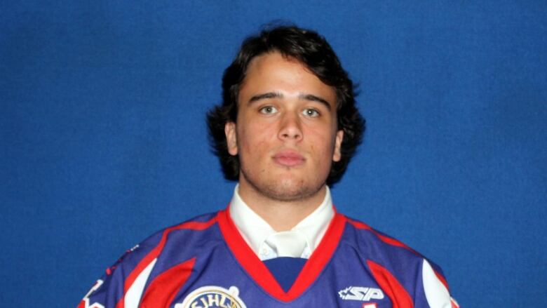 A man in a blue, red and white hockey jersey in front of a blue background.