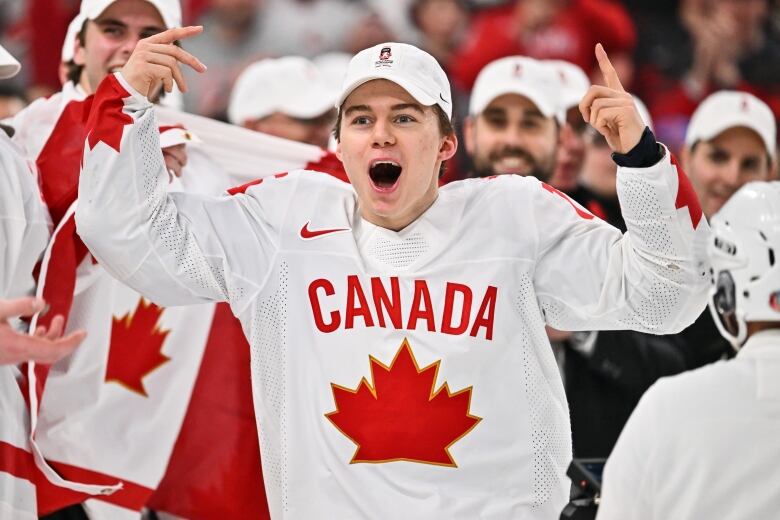 Hockey player throws his hands in the air while wearing white Team Canada jersey.