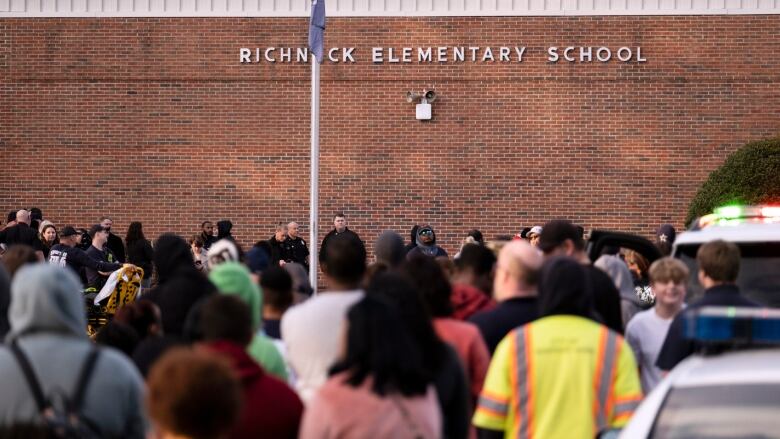 A crowd of people gather outside a school.