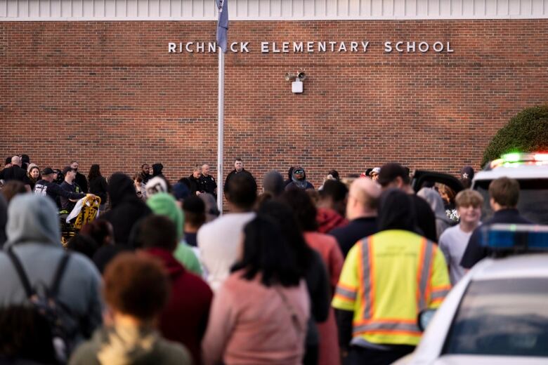 A crowd of people gather outside a school.