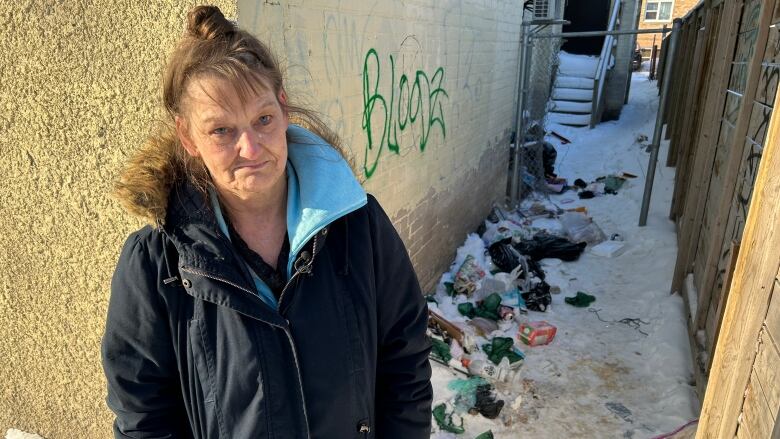 A woman stands in front of a building with piles of garbage on the ground beside it.