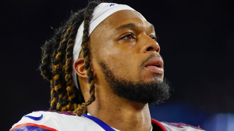 A male football player wearing a headband stands on the field without his helmet on.