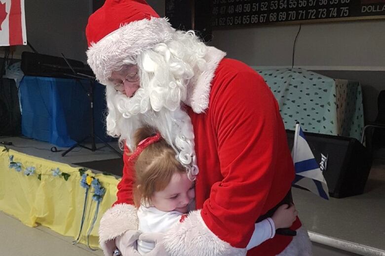 A Santa Claus figure hugs a small child who is hugging him at the waist.