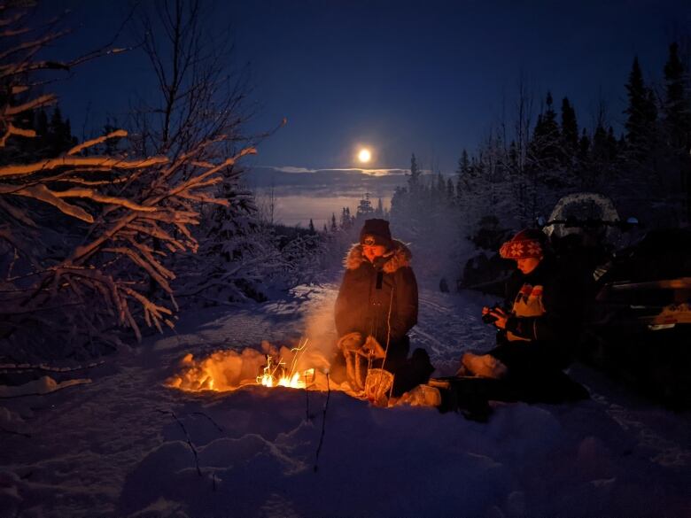 A pair of snowmobilers huddle near the fire on a snowy trail in Labrador.