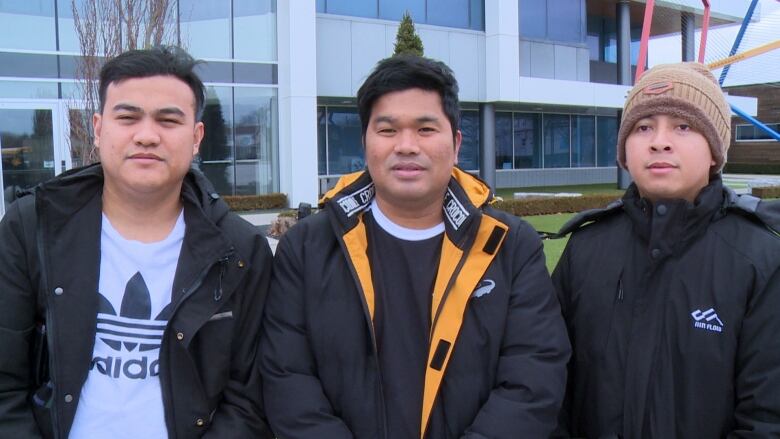 Three men with black hair wearing black jackets standing beside each other