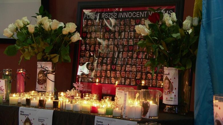 A poster board with photos of the people who died on the flight, lit by surrounding candles