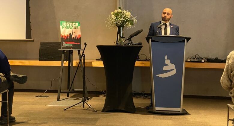 A man stands at a podium next to a sign saying 