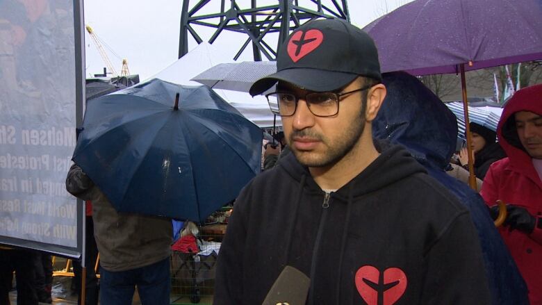 A man in a black hat with red emblem and matching sweater speaks with a reporter in North Vancouver B.C.