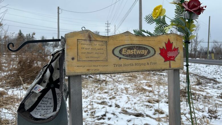 Flowers and a ball cap with writing on it hang as a memorial on a company sign.