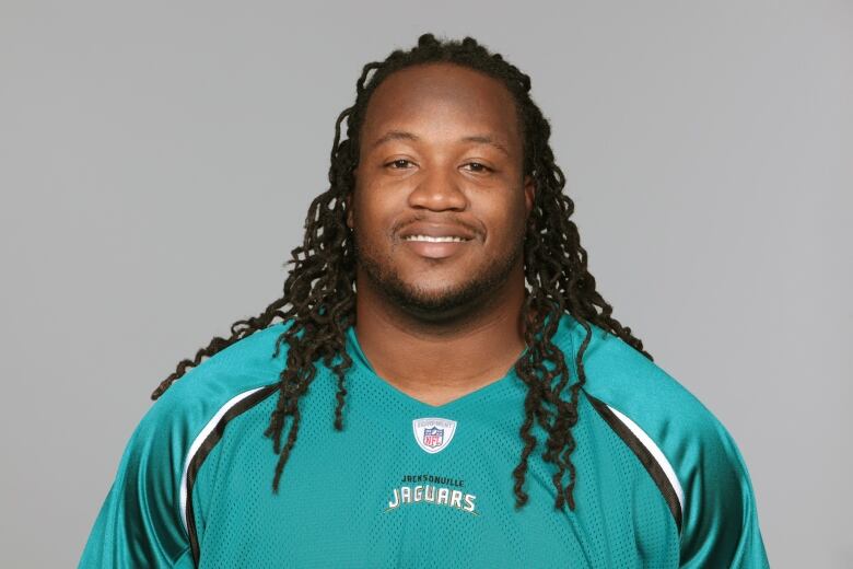 A portrait of a smiling man with long, curly braids and a Jacksonville Jaguars jersey.