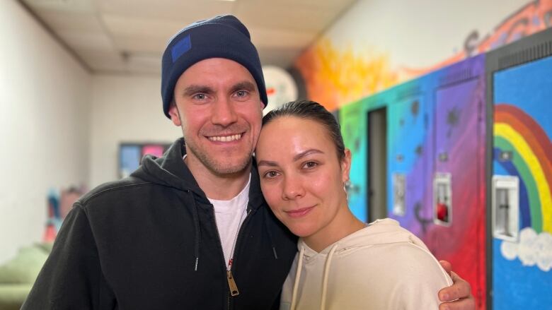 A smiling man and woman stand with their arms around each other.