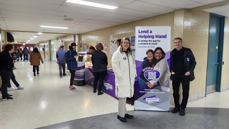 A man and a woman pose for the camera next to a banner promoting a charity drive.