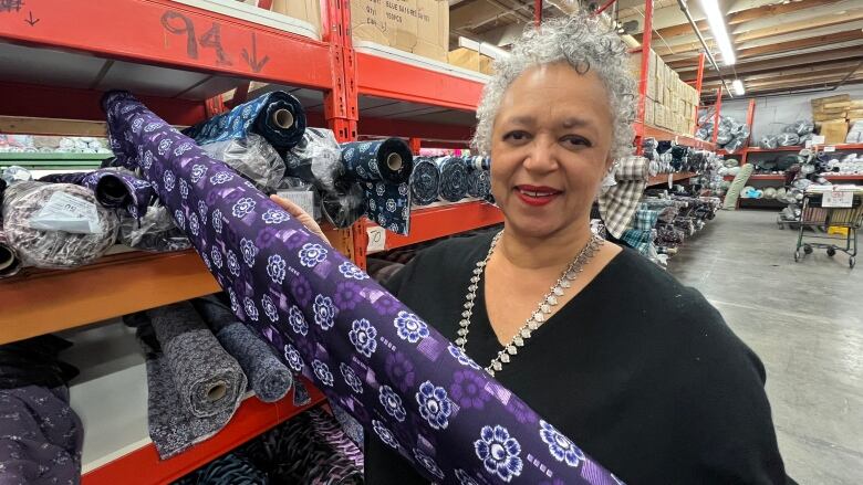 A woman with curly hair looks at the camera while holding a roll of fabric