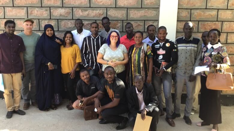 About twenty people are shown standing together with a wall behind them in Kenya. Some are hoping to move to Nova Scotia to work in long-term care.