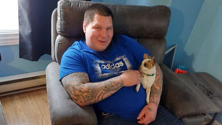 An Indigenous man holds a dog, as he wears a blue shirt. 