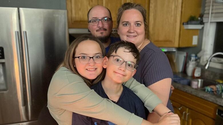 A family hugs and poses for a photo in their kitchen.