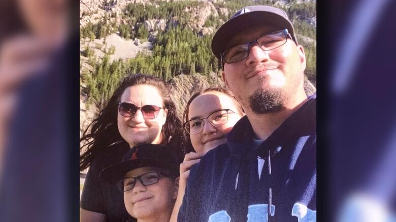 A family poses for a photo outside with a forest in the background.