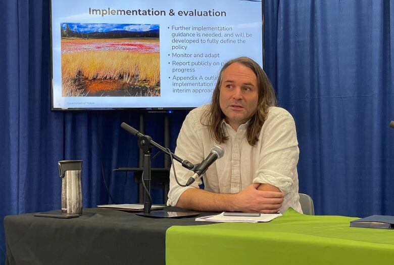 A man sits as a table before a microphone.