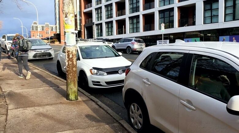 A person in a colourful coat walks up the street beside a row of parked cars