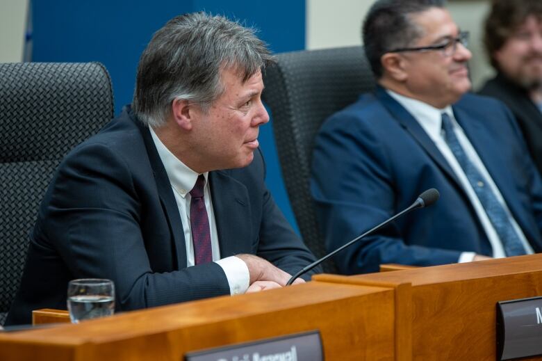 A man sits at a desk and listens to someone speaking.