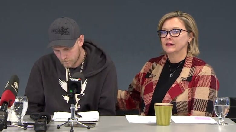 Three people sit at a table in front of microphones.